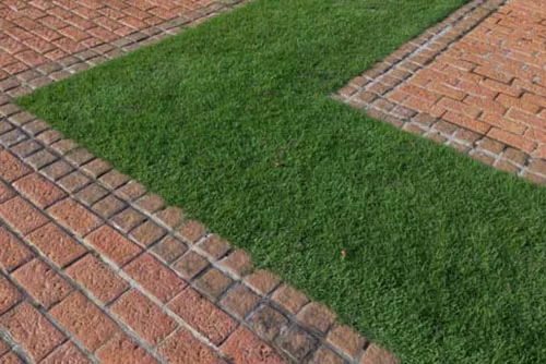 A geometric pattern of red brick paths and green grass sections. The image shows intersecting pathways, creating a visually appealing design of alternating brick and grass.